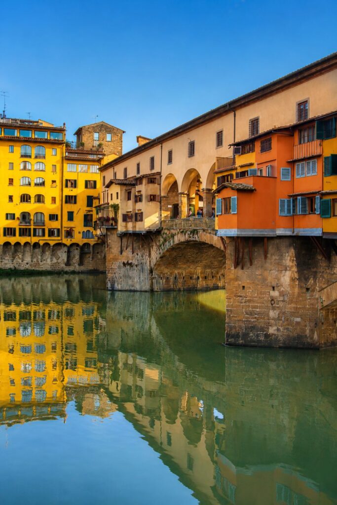 Ponte Vecchio with colorful bridge shops reflected in the calm green Arno River