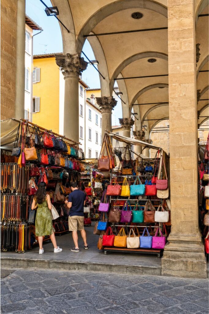 Colorful leather bags displayed under stone arches at San Lorenzo Market in Florence