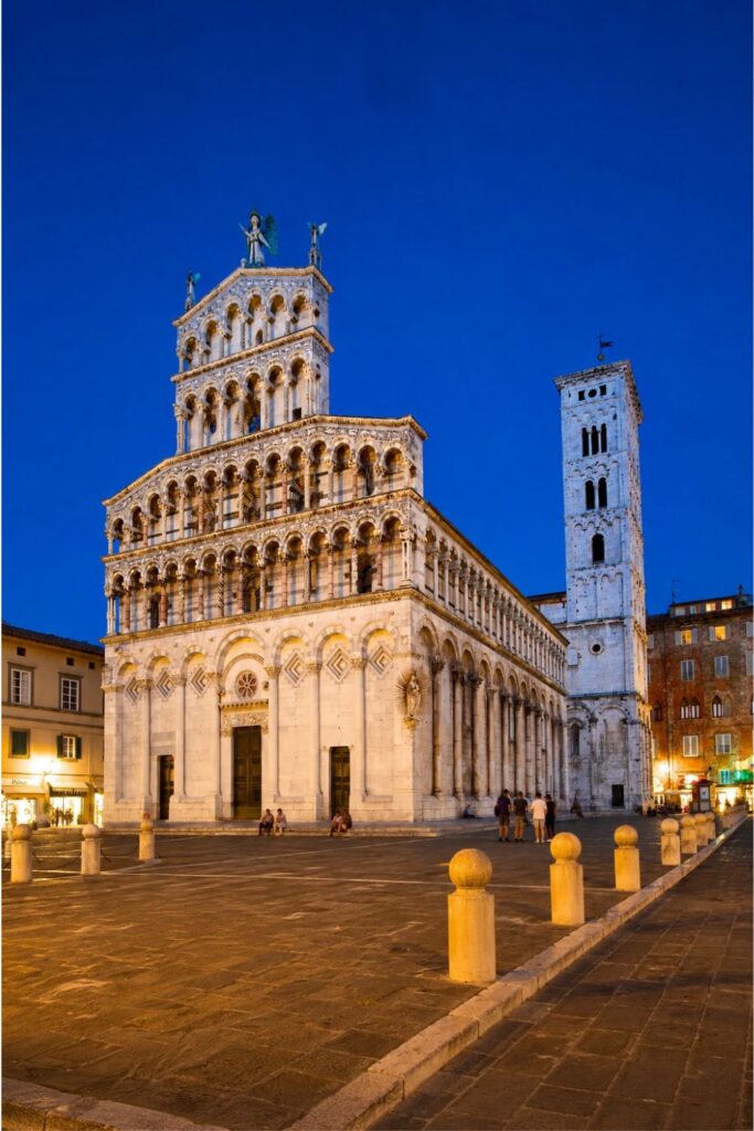 Lucca cathedral and bell tower glowing at blue hour in a quiet stone piazza