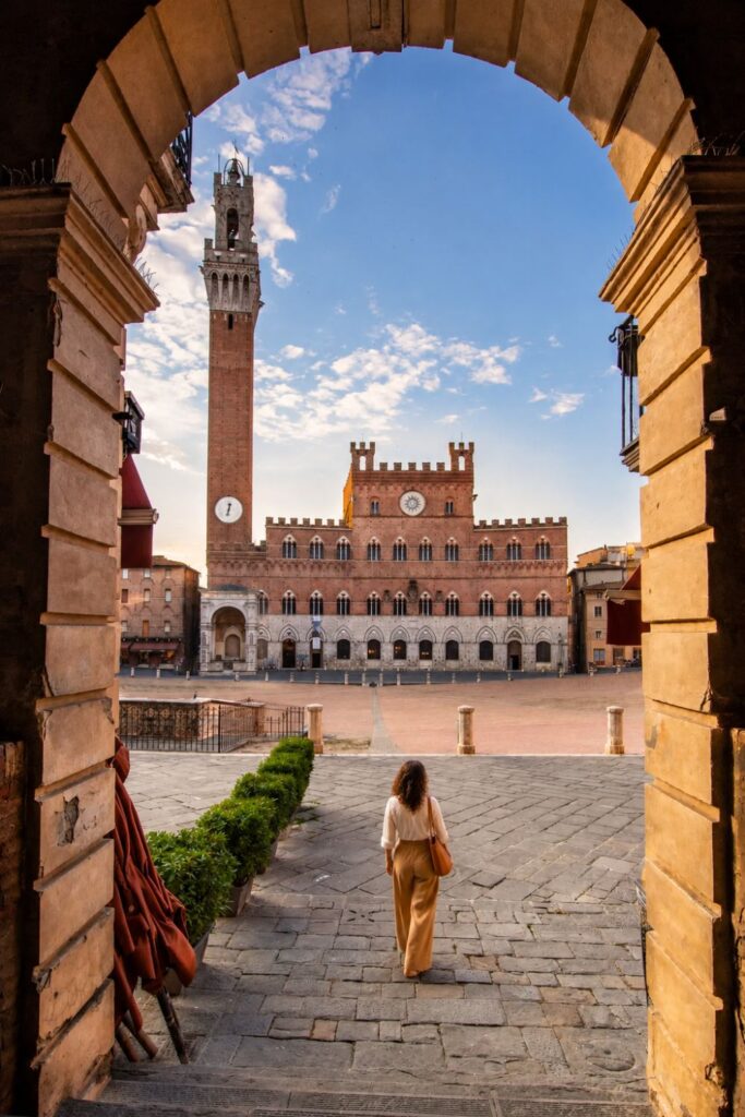 Stone arch framing Siena’s Piazza del Campo, Torre del Mangia, and medieval palace at sunset