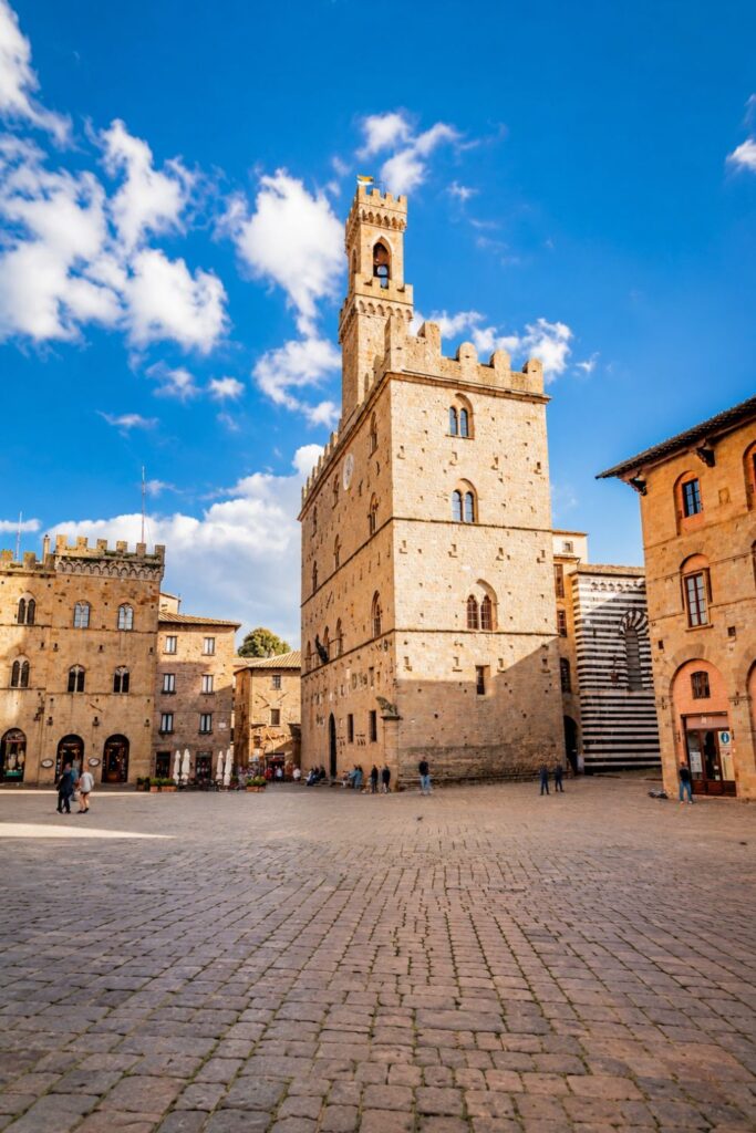 Wide stone piazza in Volterra with medieval palace, tower, and warm Tuscan facades