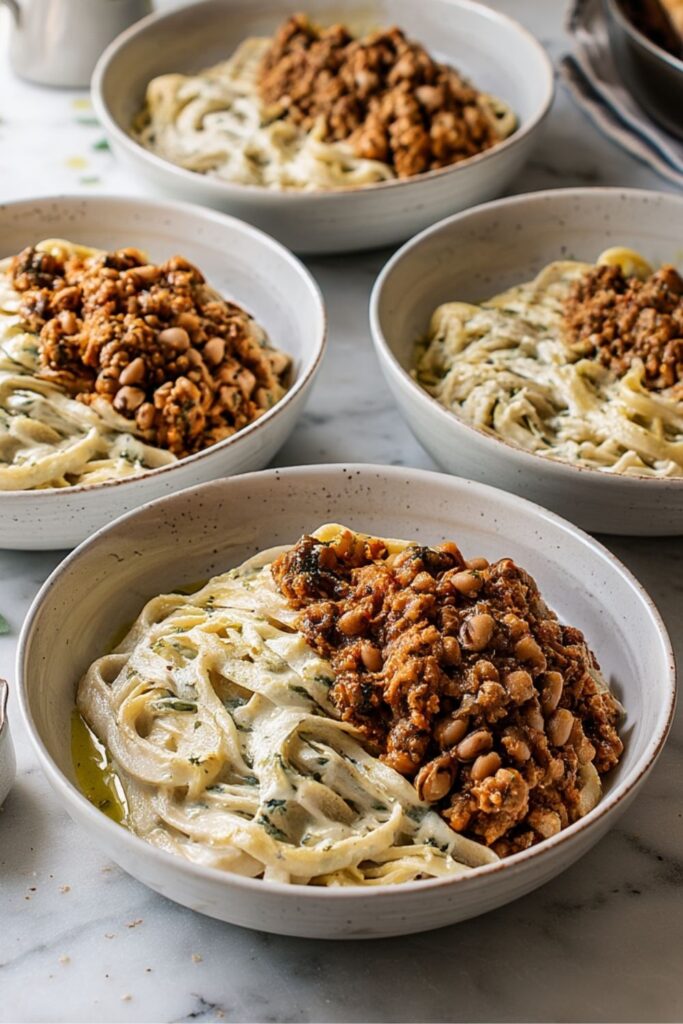 Four bowls filled with creamy pasta, beans, and seasoned tripe on a surface.