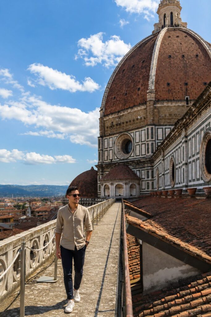 A traveler walks the Duomo rooftop terrace beside Brunelleschi’s dome under a bright blue sky.