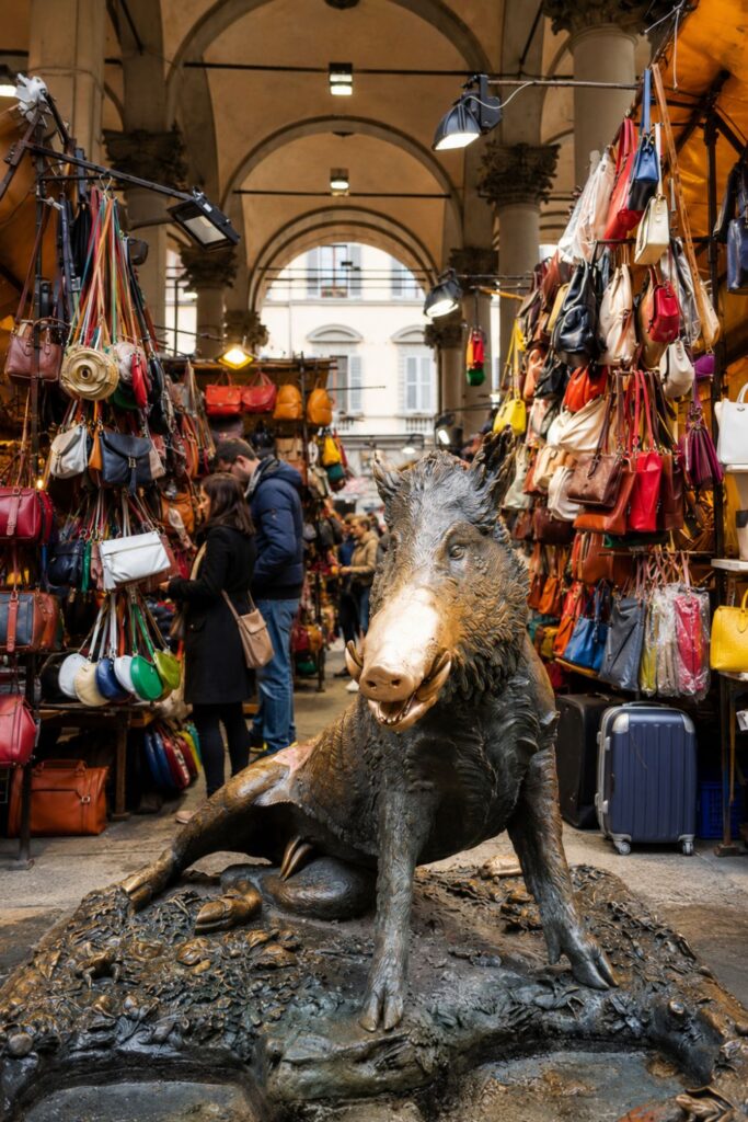 Bronze Porcellino statue framed by colorful leather stalls beneath Florence’s market arches.