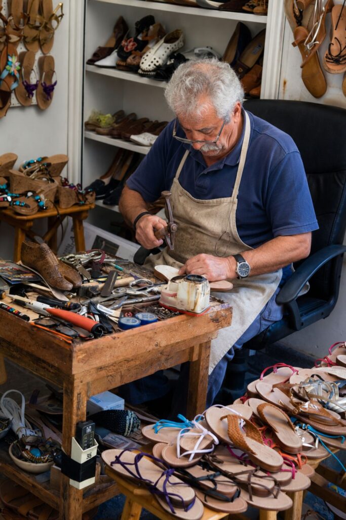An artisan shapes leather sandals at a tool-covered workbench in Florence’s Oltrarno district.