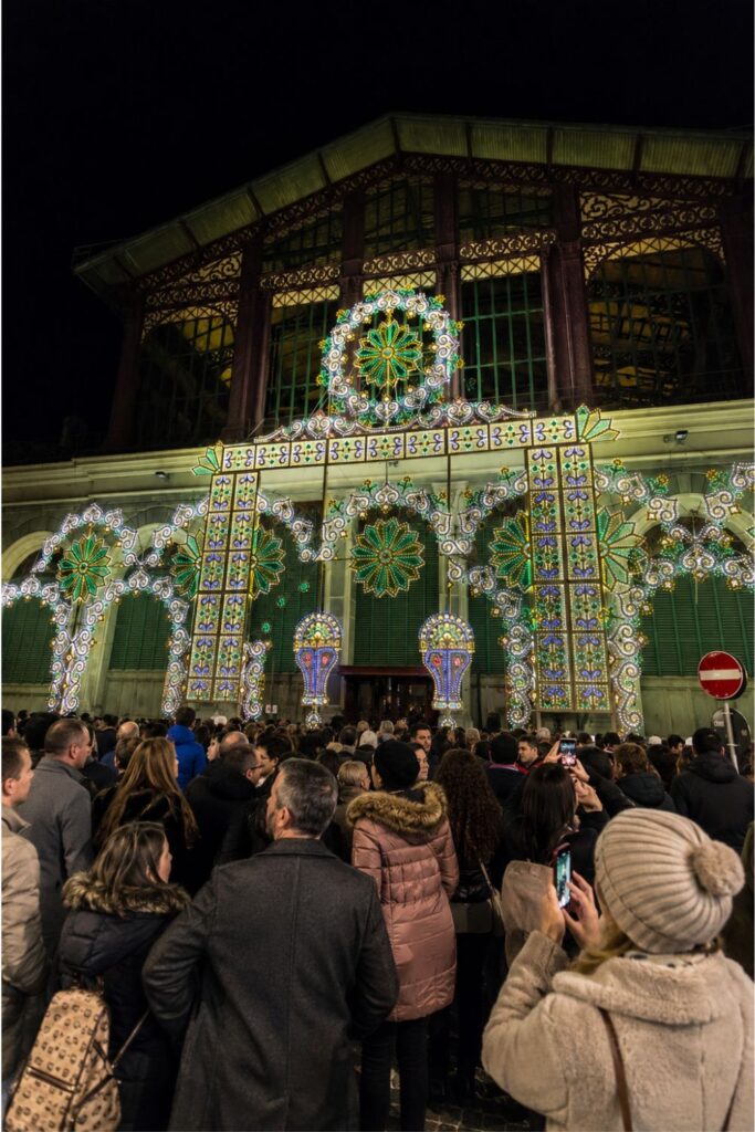 Holiday lights cover Mercato Centrale’s facade as a winter crowd gathers beneath the arches.