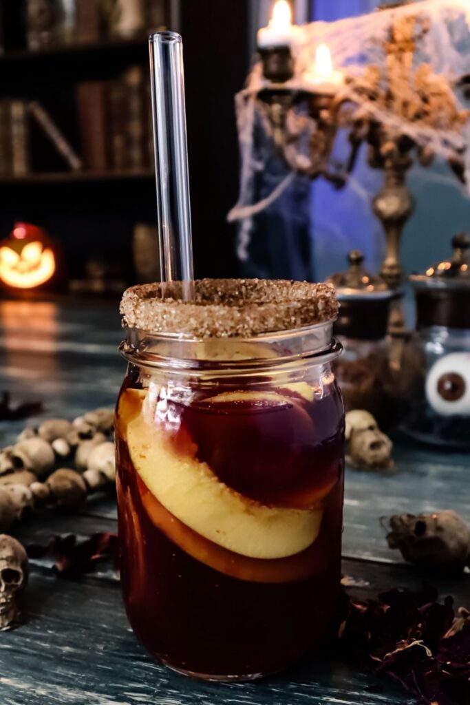 A mason jar filled with spiced apple cider, apple slices, and a sugar rim.