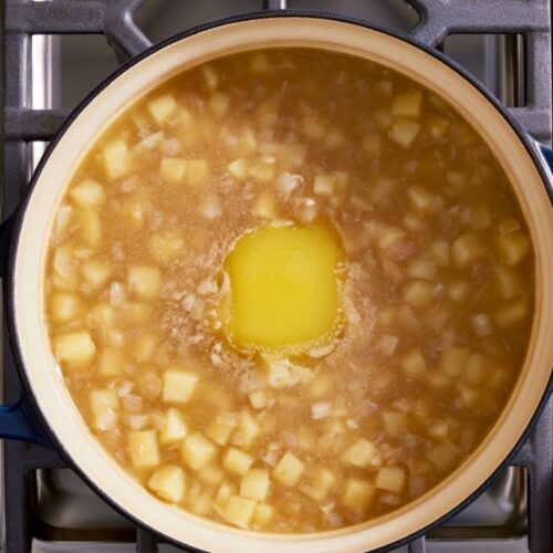 Overhead view of diced potatoes and melted butter in a pot on a stove.