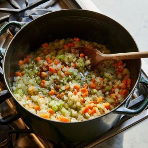Dark-green Dutch oven with sautéed carrots, celery, onions, and pancetta on a gas stovetop.