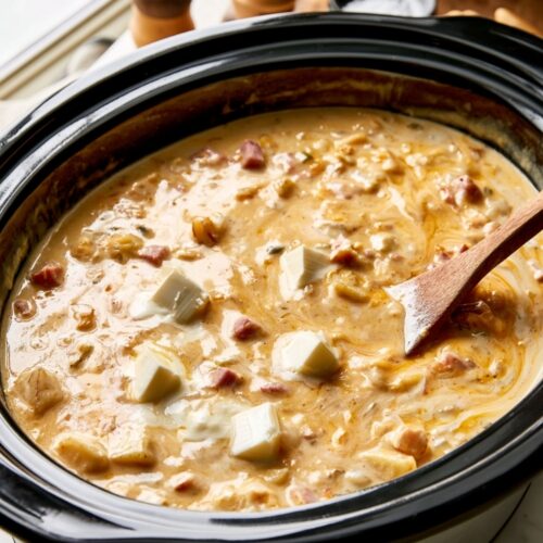 Cream cheese cubes floating in a creamy soup base inside a slow cooker.