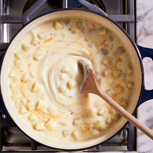 Overhead view of a wooden spoon stirring creamy potato soup in a pot.