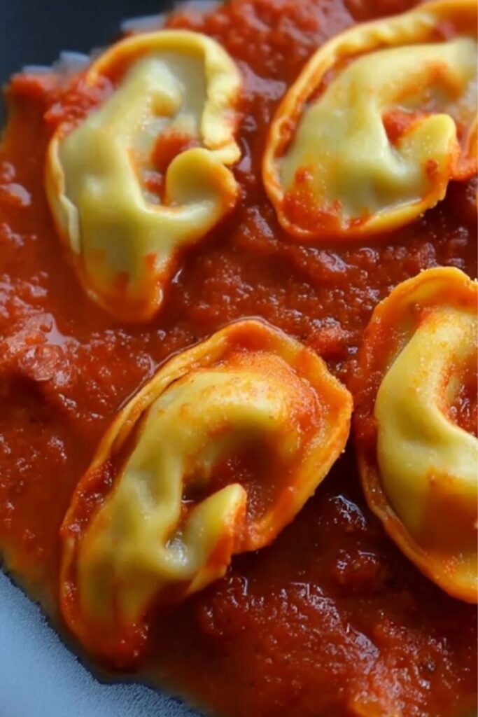 Homemade ear-shaped ravioli filled with ground beef served over red tomato sauce.