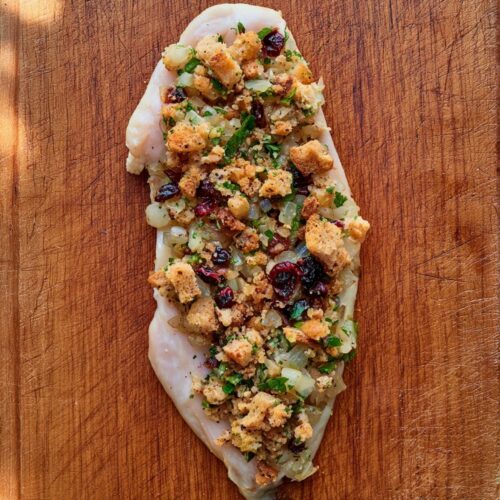 A thin chicken cutlet topped with a savory breadcrumb and cranberry stuffing on a wooden board.