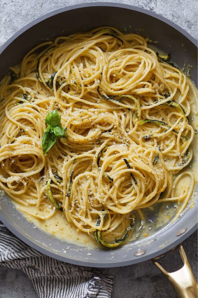 Spaghetti tossed with fried zucchini and melted cheese in a pan.