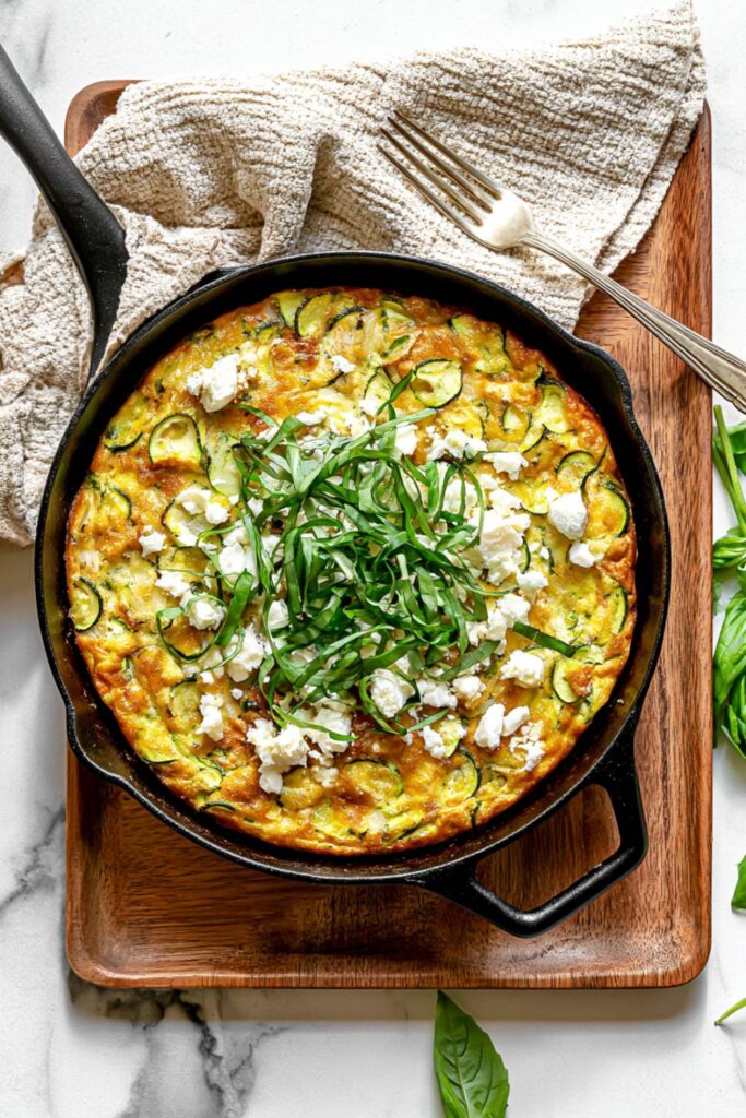 Cast-iron skillet frittata loaded with zucchini half moons, crumbled feta cheese, and fresh basil ribbons.